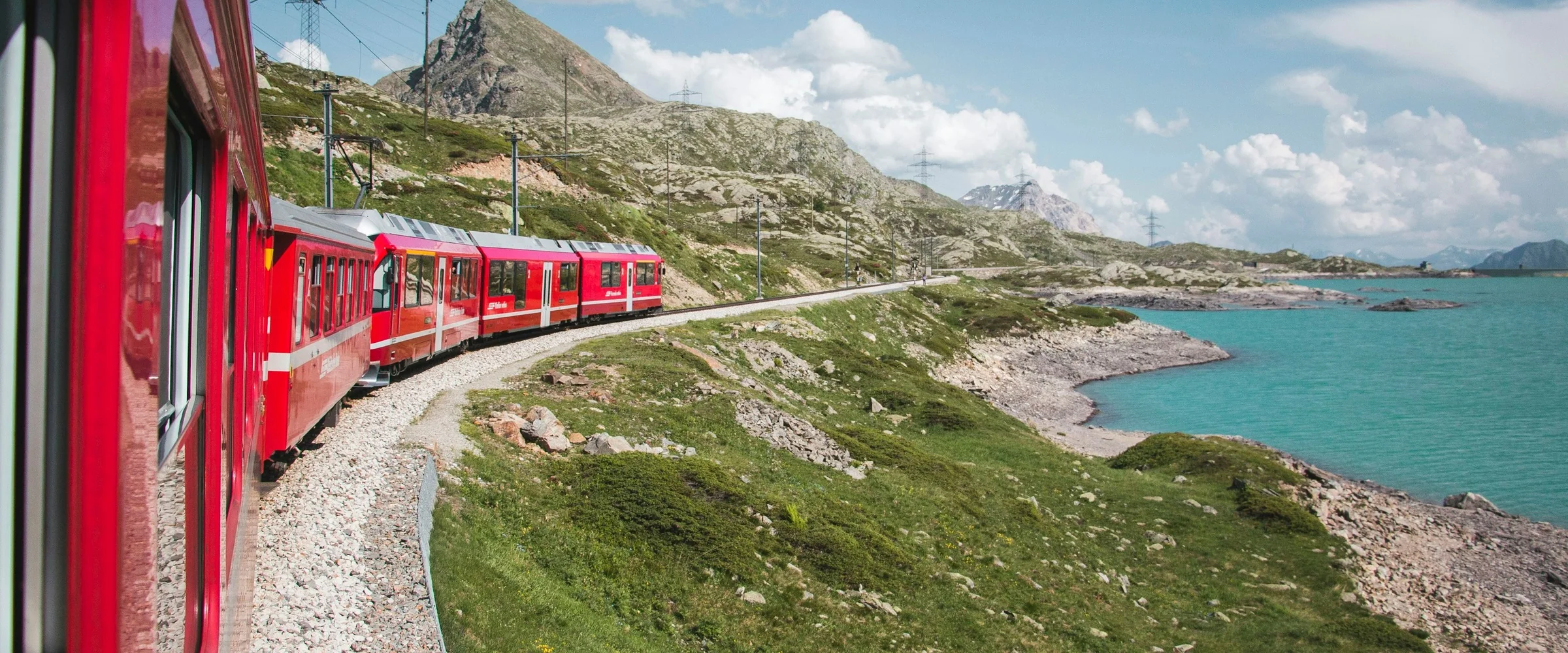 A red electric passenger train curves beside a turquoise alpine lake.