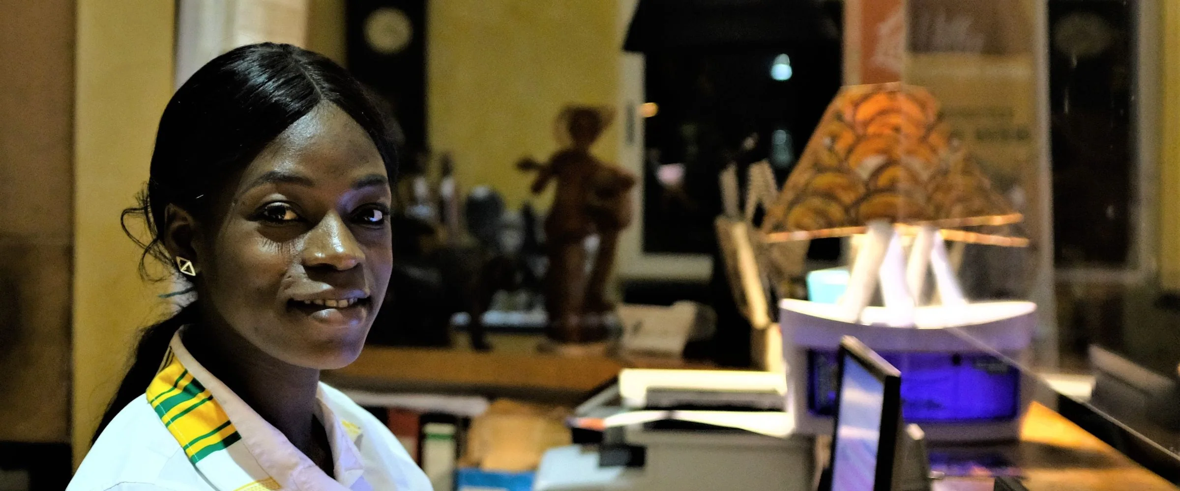A hotel receptionist in Accra smiles beside the computers at her desk.